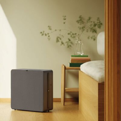 Airthings Renew air purifier on a wood floor beside a bed